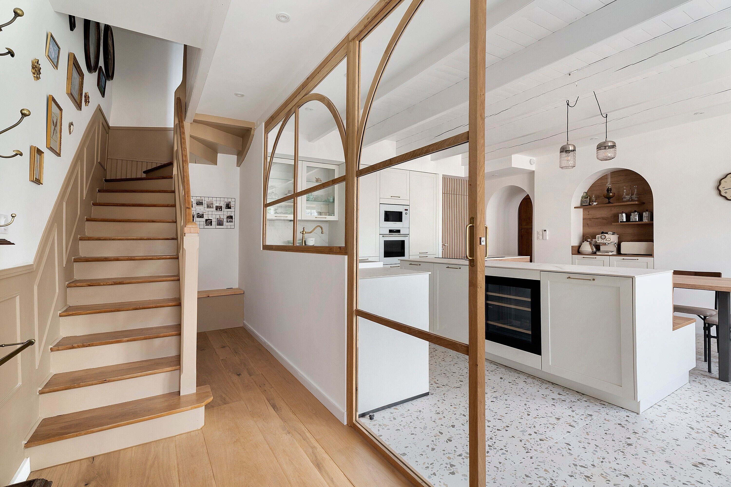 A modern kitchen with a central island, wooden staircase, and a view into the dining area.