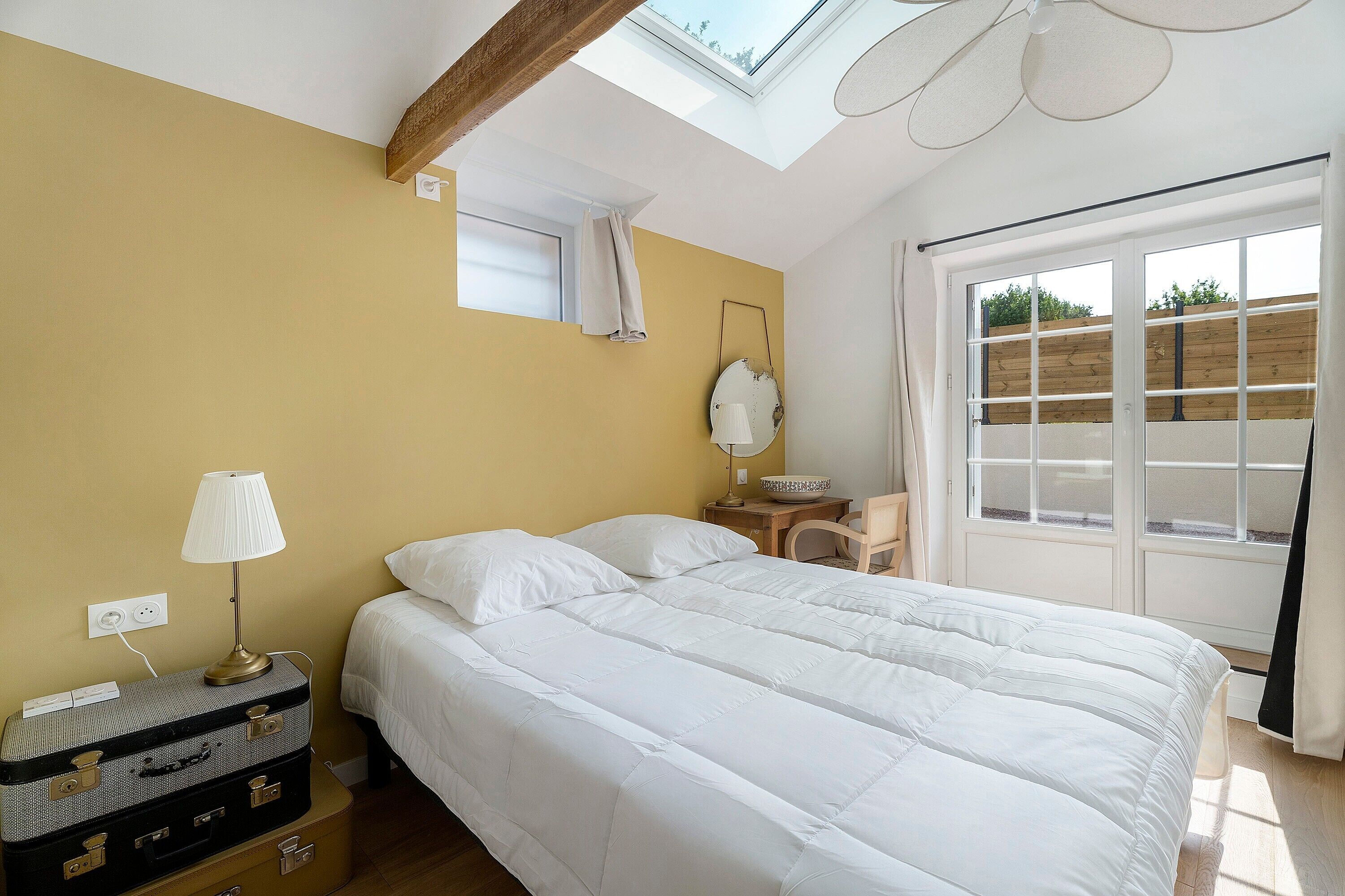 Une chambre à coucher avec un lit, une lampe, un miroir, une fenêtre et une lucarne.