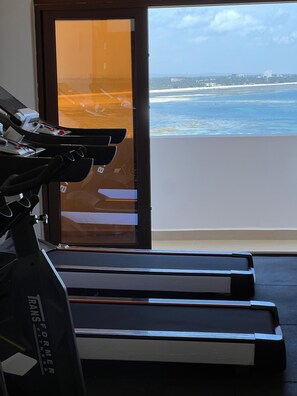 A treadmill and a sliding glass door leading to a balcony with a view of the ocean and cityscape. - Luxury Living in Nyali — Wake up to breathtaking ocean view (Mombasa)