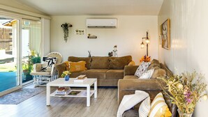 Uma sala de estar com sofá marrom, mesa de centro branca e porta de vidro que dá para área externa.