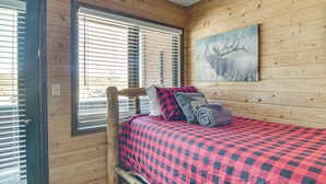 A wooden cabin room with a bed, a window with blinds, and a painting on the wall. - < 1 Mi to Granby Rodeo! Retreat w/ Pool & Hot Tub (Granby)