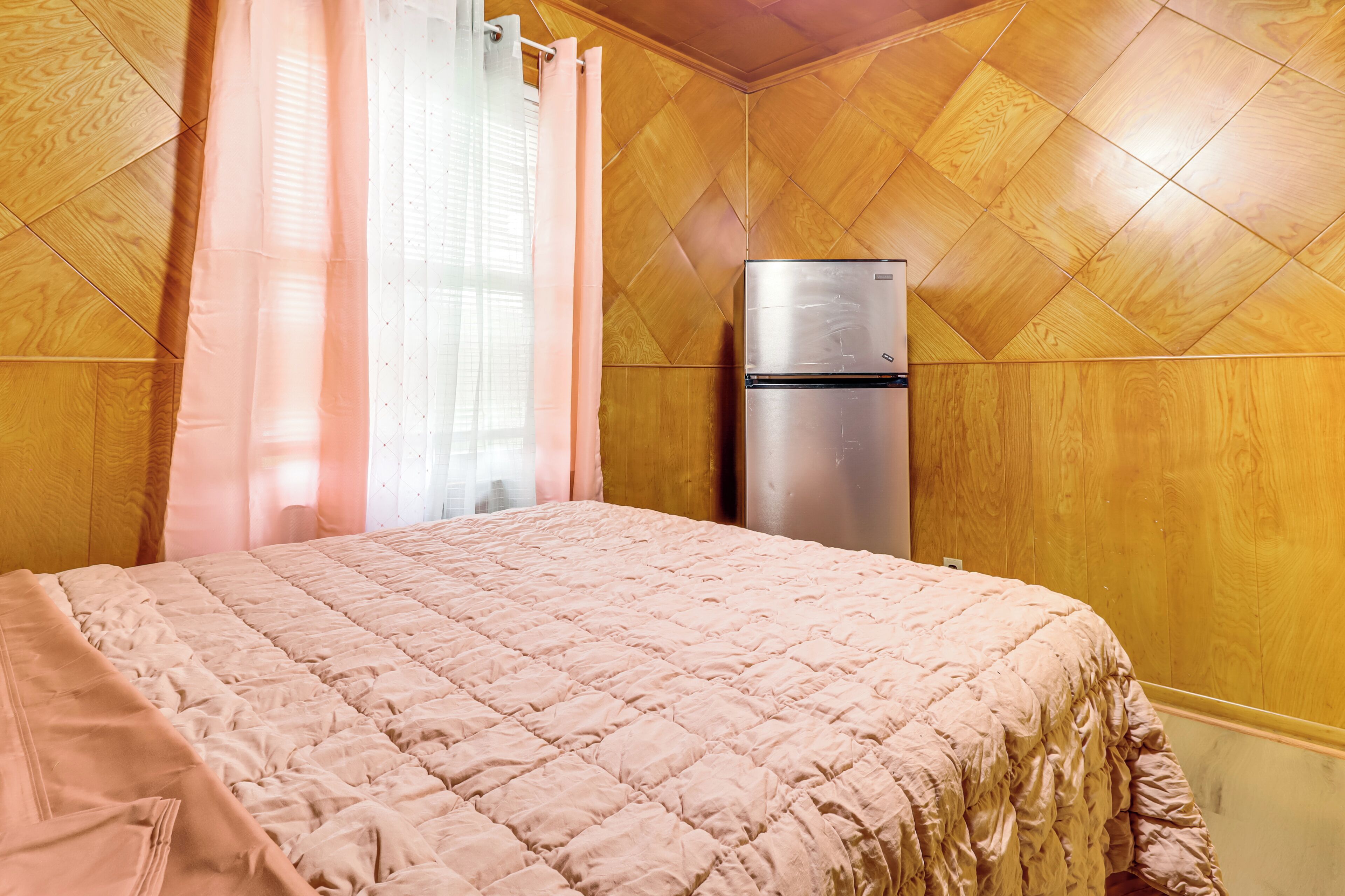 Een kamer met een bed, een koelkast, houten lambrisering en een raam met gordijnen.
