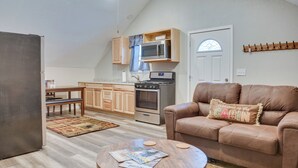 A cozy living room with a brown leather sofa, a wooden coffee table, and a kitchen area with wooden cabinets and a microwave.