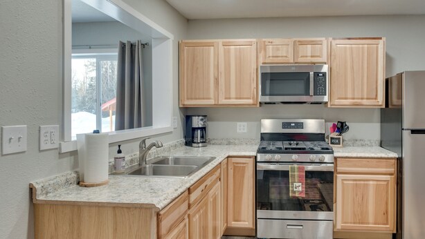 A modern kitchen with wooden cabinets, stainless steel appliances, a granite countertop, and a window with curtains.