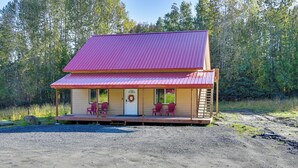 A two-story building with a red roof, a porch with chairs, and a door with a wreath.