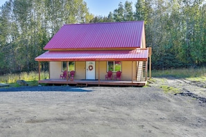 A two-story building with a red roof, a porch with chairs, and a door with a wreath. - Kenai River Base! Spacious 2-unit Cabin Compound (Soldotna)