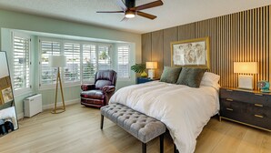 A bedroom with a bed, a ceiling fan, a bench, a chair, a bedside table with lamps, and a wall-mounted artwork. - Luxe Detached Home in Age 55 Plus Active Community (Sun City West)