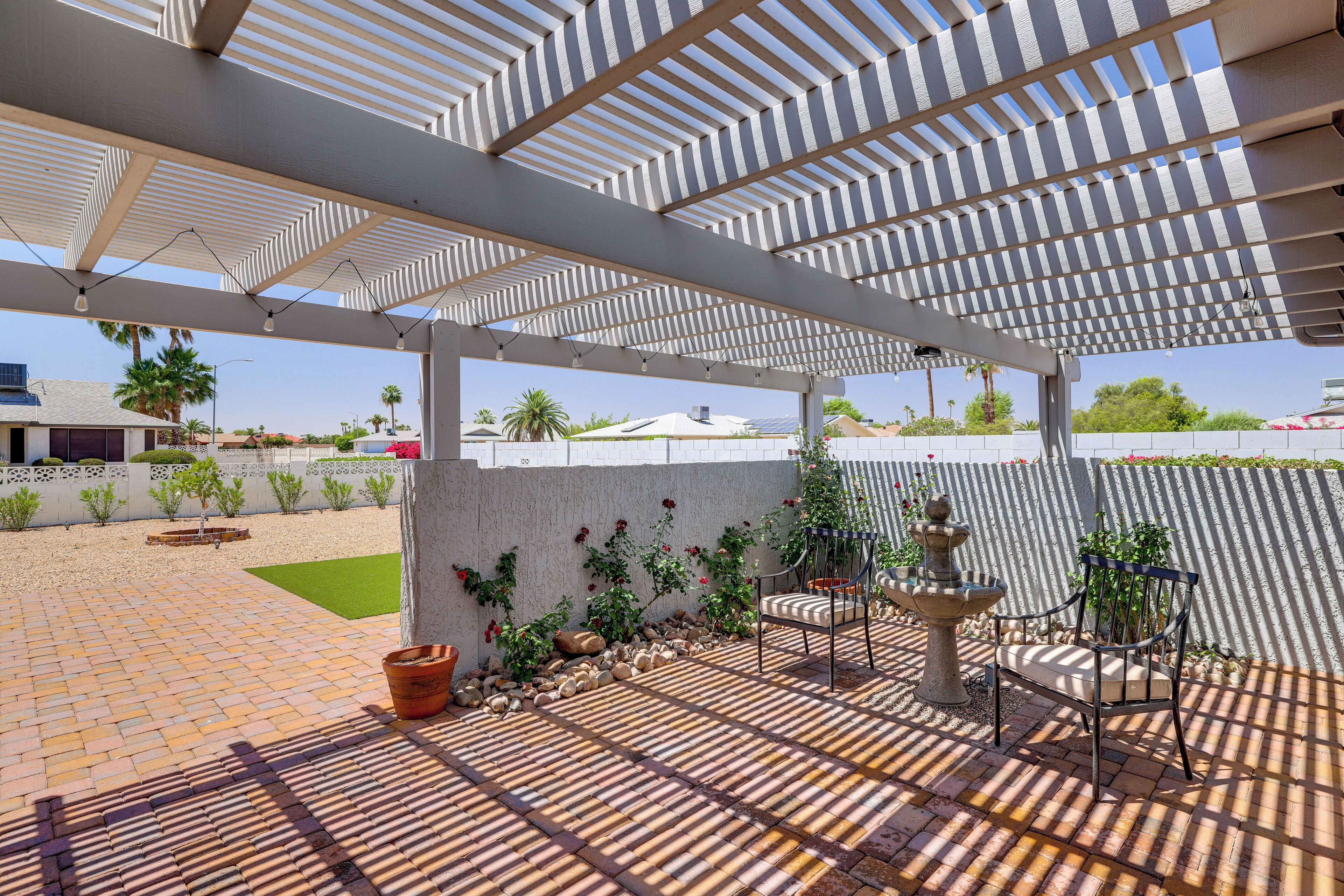 A covered patio area with a pergola, outdoor seating, a water feature, and a view of the surrounding landscape.