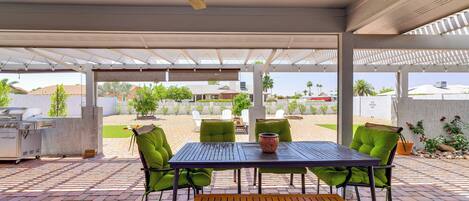 Eine Terrasse im Freien mit Tisch, Stühlen, Deckenventilator und Grill.