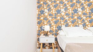 Una camera da letto con carta da parati floreale, un comodino con lampada e un letto con biancheria bianca.