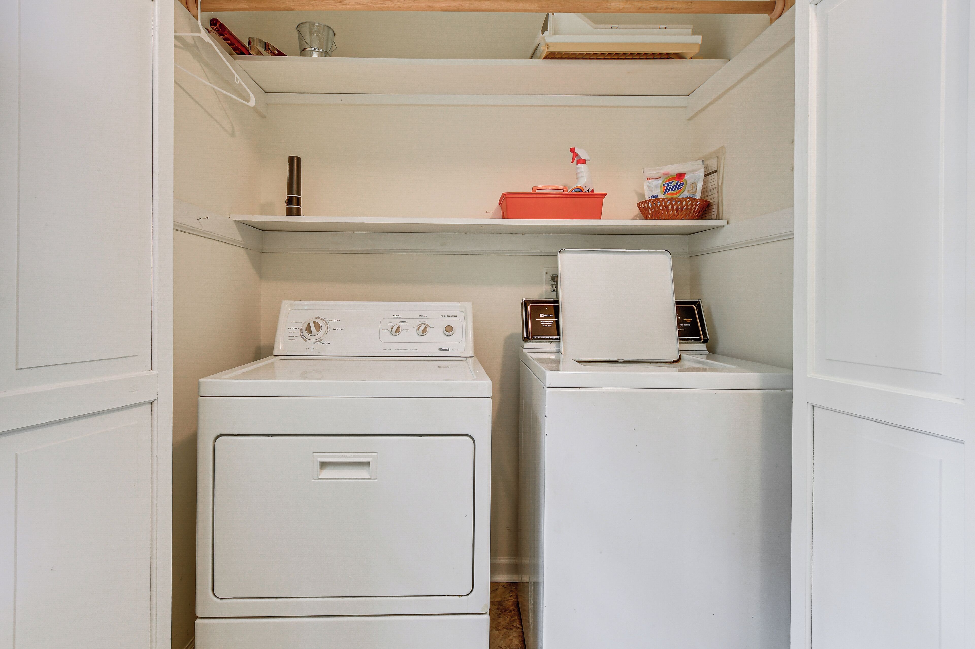 A laundry room with two stacked washers and dryers, a shelf with laundry supplies, and a small basket.
