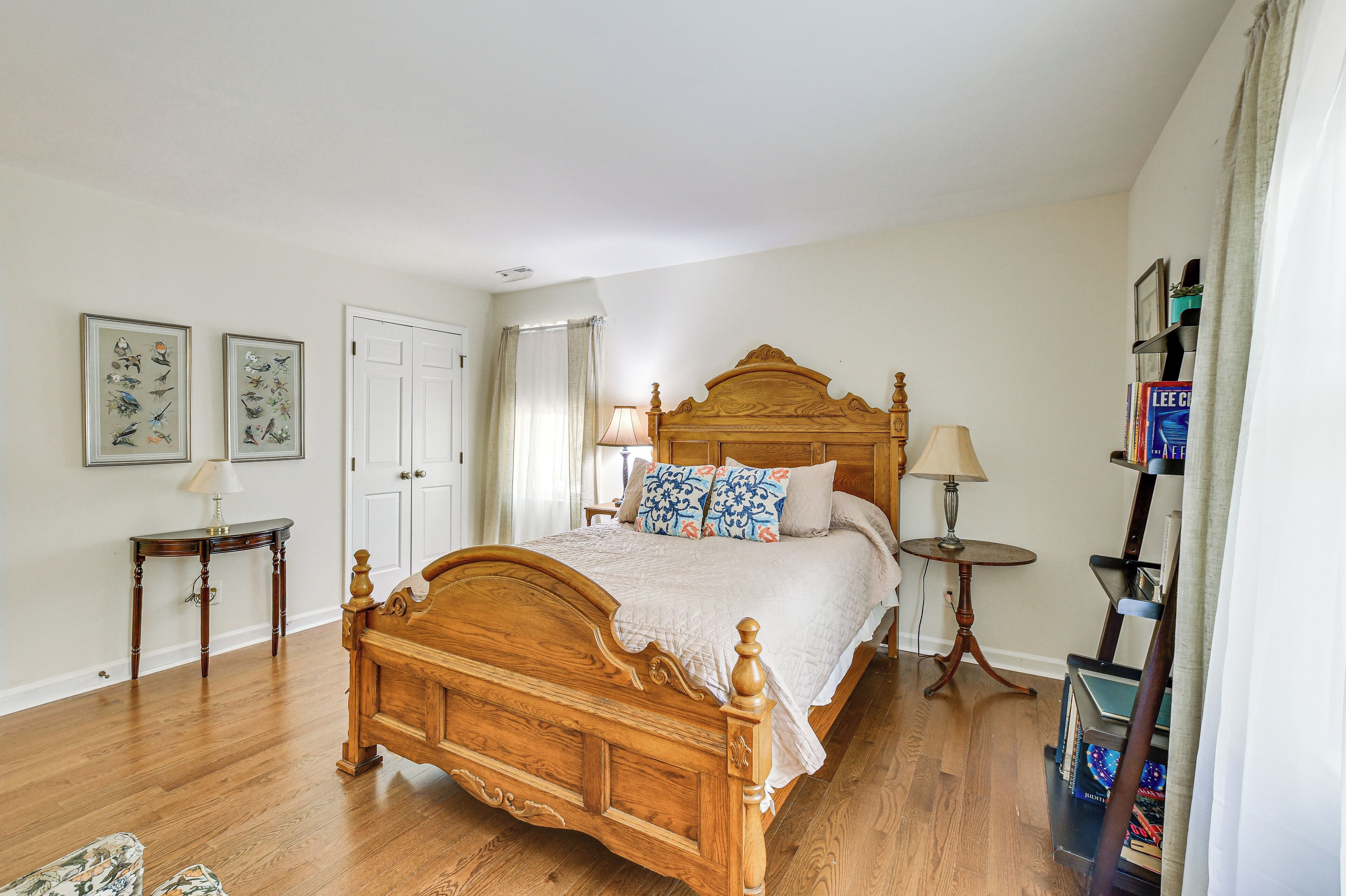 Un dormitorio con una cama de madera, dos mesitas de noche, una mesita auxiliar, una estantería y una puerta.