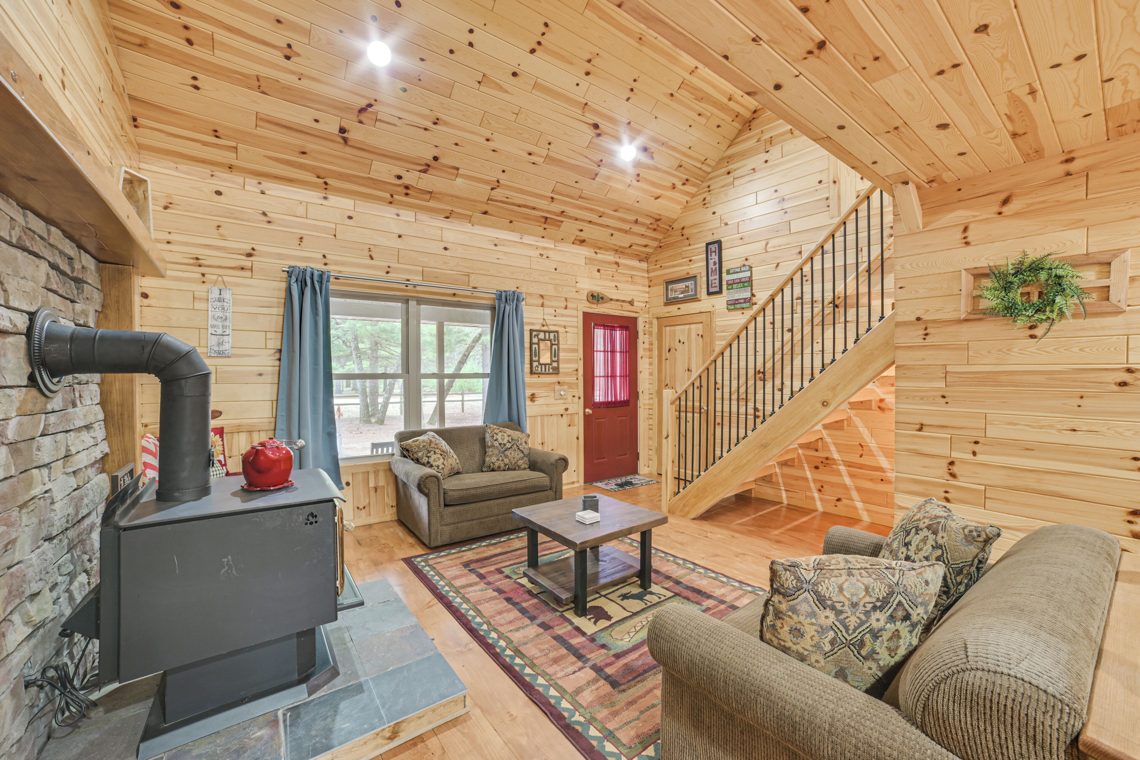 A wooden cabin interior with a fireplace, a staircase, a sofa, and a coffee table.