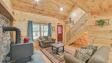 A wooden cabin interior with a fireplace, a staircase, a sofa, and a coffee table.