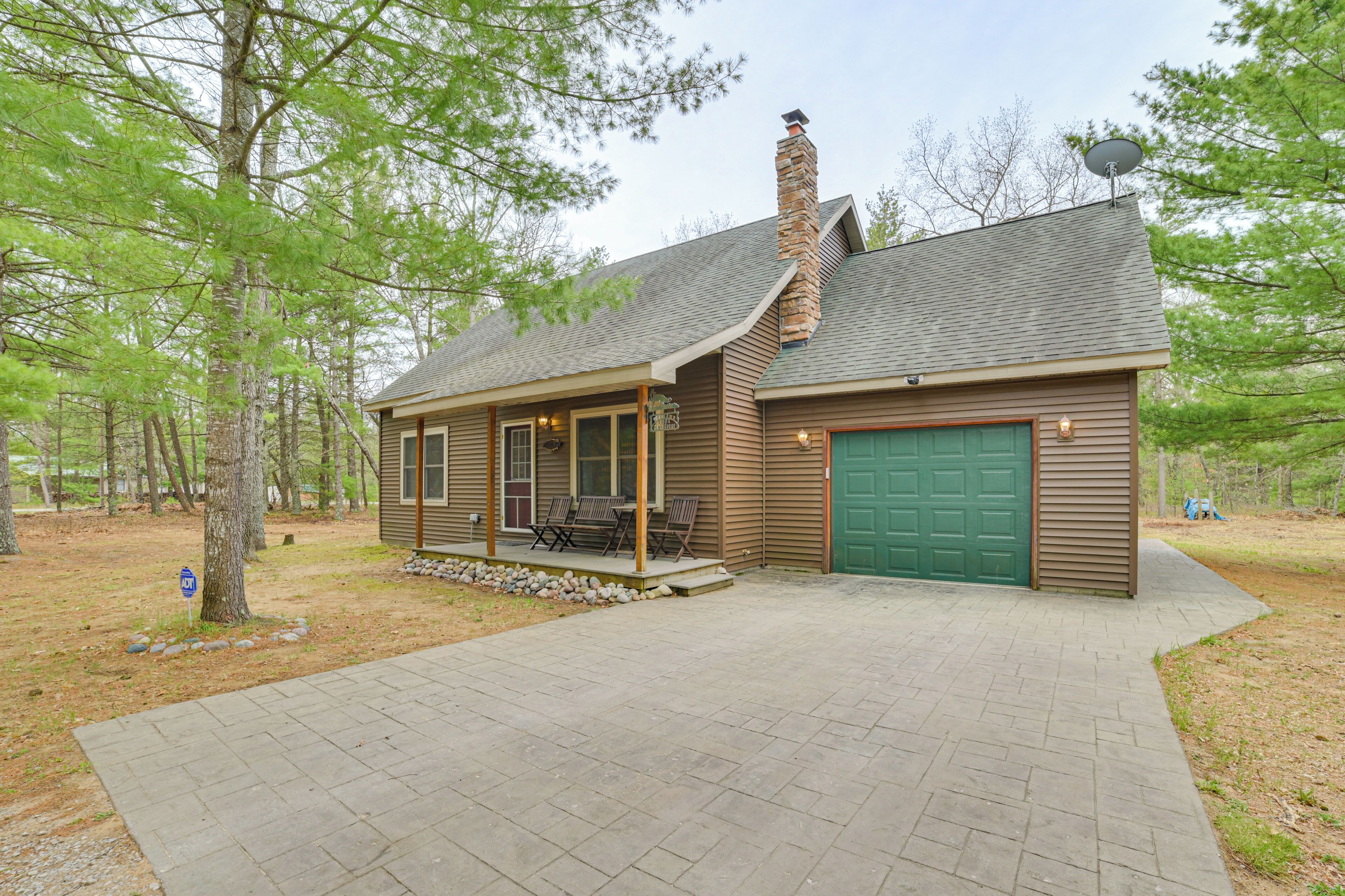A cabin with a covered porch, a chimney, and a green garage door.