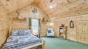 Quarto de cabana de toras com uma cama, uma cadeira, uma estante e uma janela.
