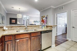 A kitchen with granite countertops, a dishwasher, wooden cabinets, a pendant light, and a painting on the wall. - Disney Magic & Tuscana Resort Fun! Family Condo (Davenport)