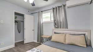 Ein Schlafzimmer mit Bett, Deckenventilator, Klimaanlage, Fenster mit Vorhängen, Nachttisch und Kleiderschrank.