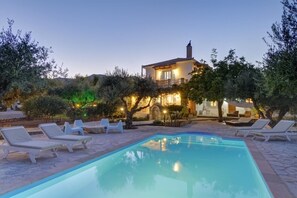 Ein Pool mit Liegestühlen, ein Haus mit Balkon und umliegende Grünflächen.