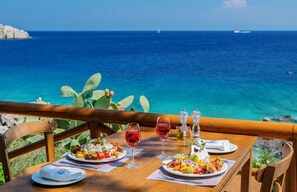 Ein Tisch mit Speisen und Weingläsern, mit Blick auf das klare, blaue Meer.