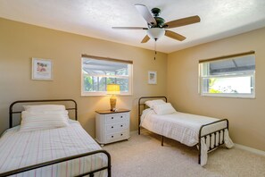 Ein Schlafzimmer mit zwei Einzelbetten, einem Deckenventilator, einem Nachttisch mit Lampe und zwei Fenstern.