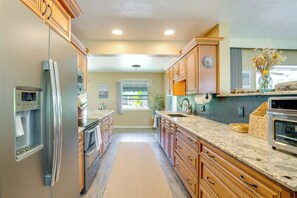 Eine Küche mit Holzausstattung, einem Edelstahlkühlschrank, einer Granitarbeitsplatte und einem eingebauten Backofen.