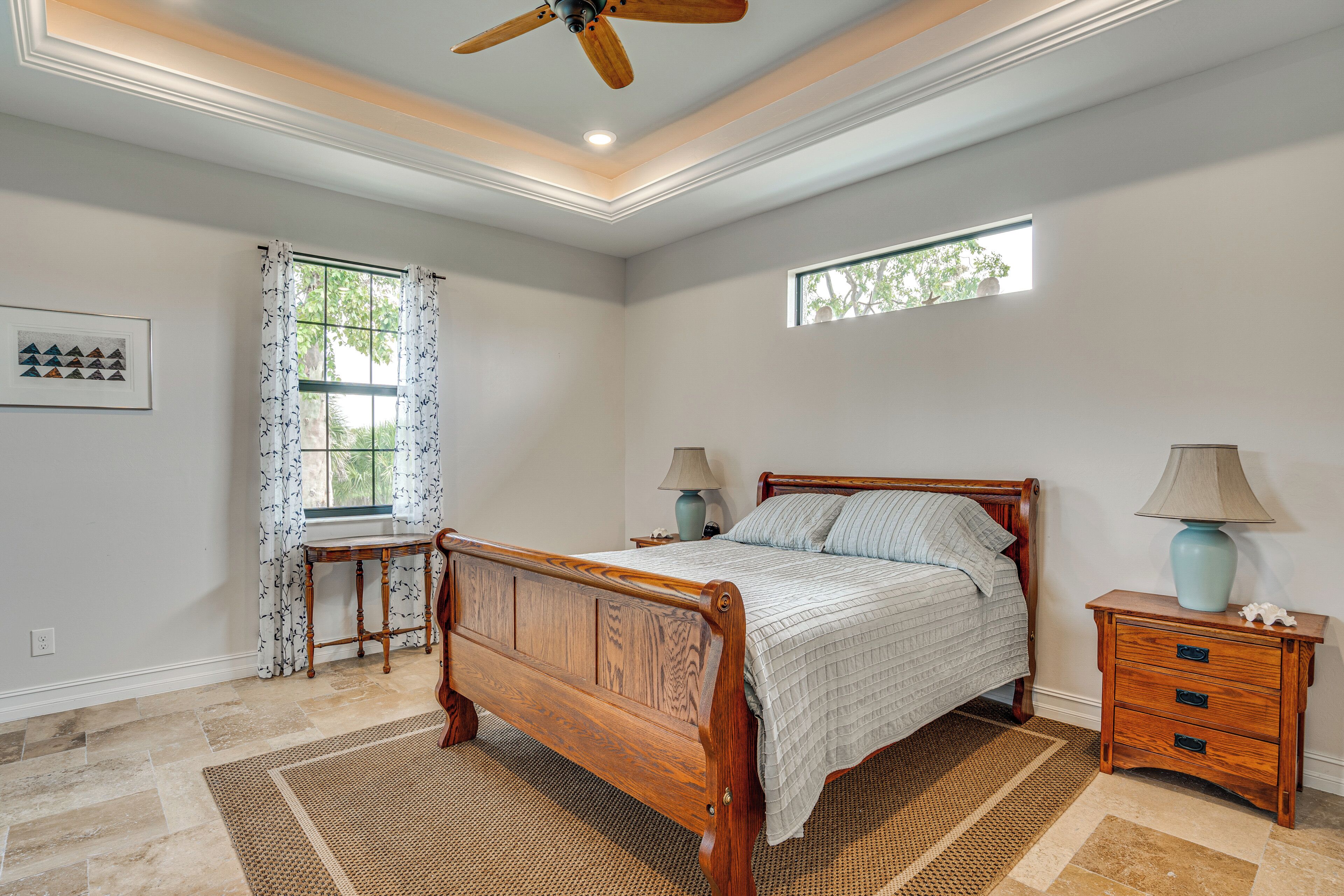A bedroom with a wooden bed, two bedside tables, a ceiling fan, a window, and a rug.