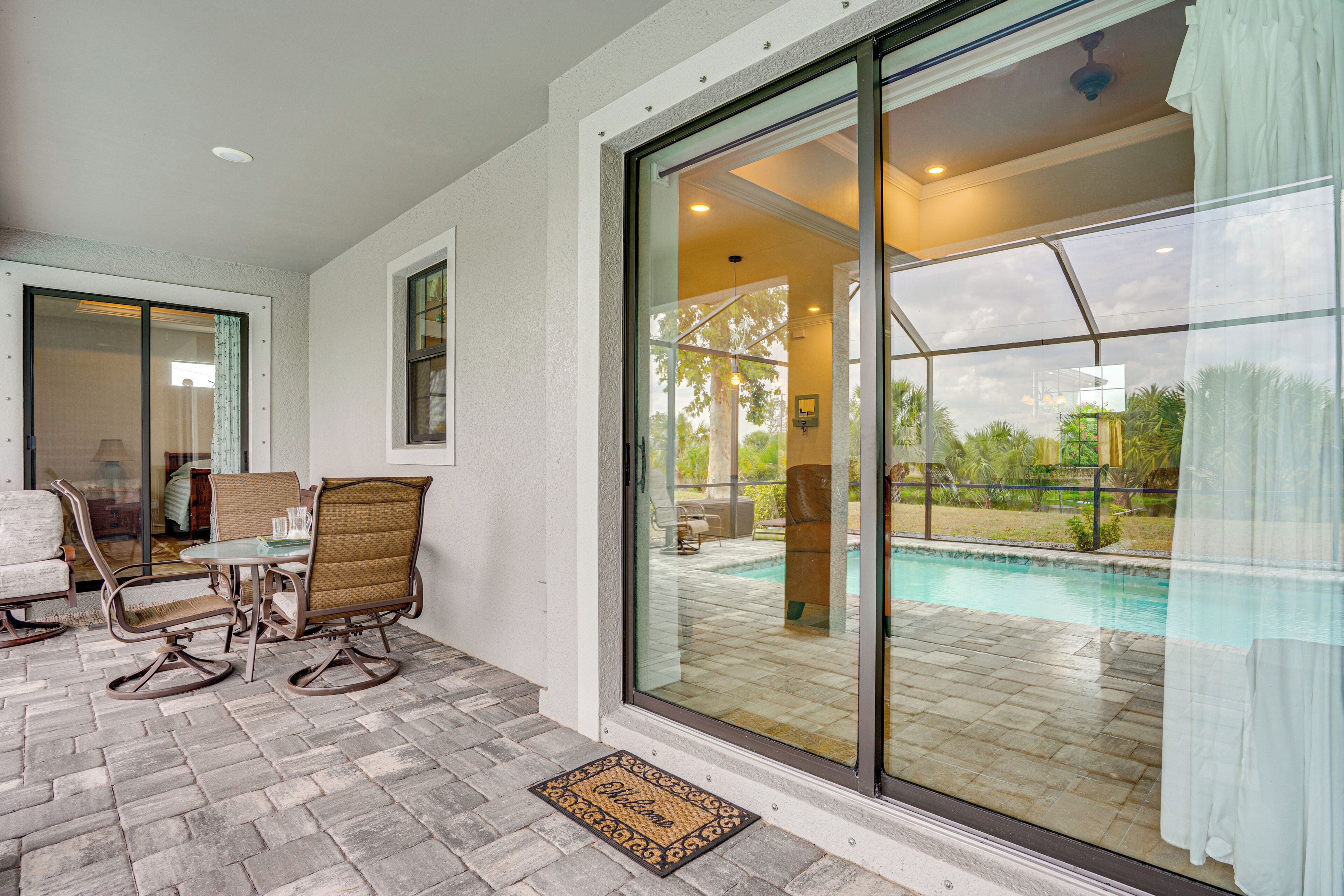 A patio with a table and chairs, a glass door leading to a pool area, and a doormat.