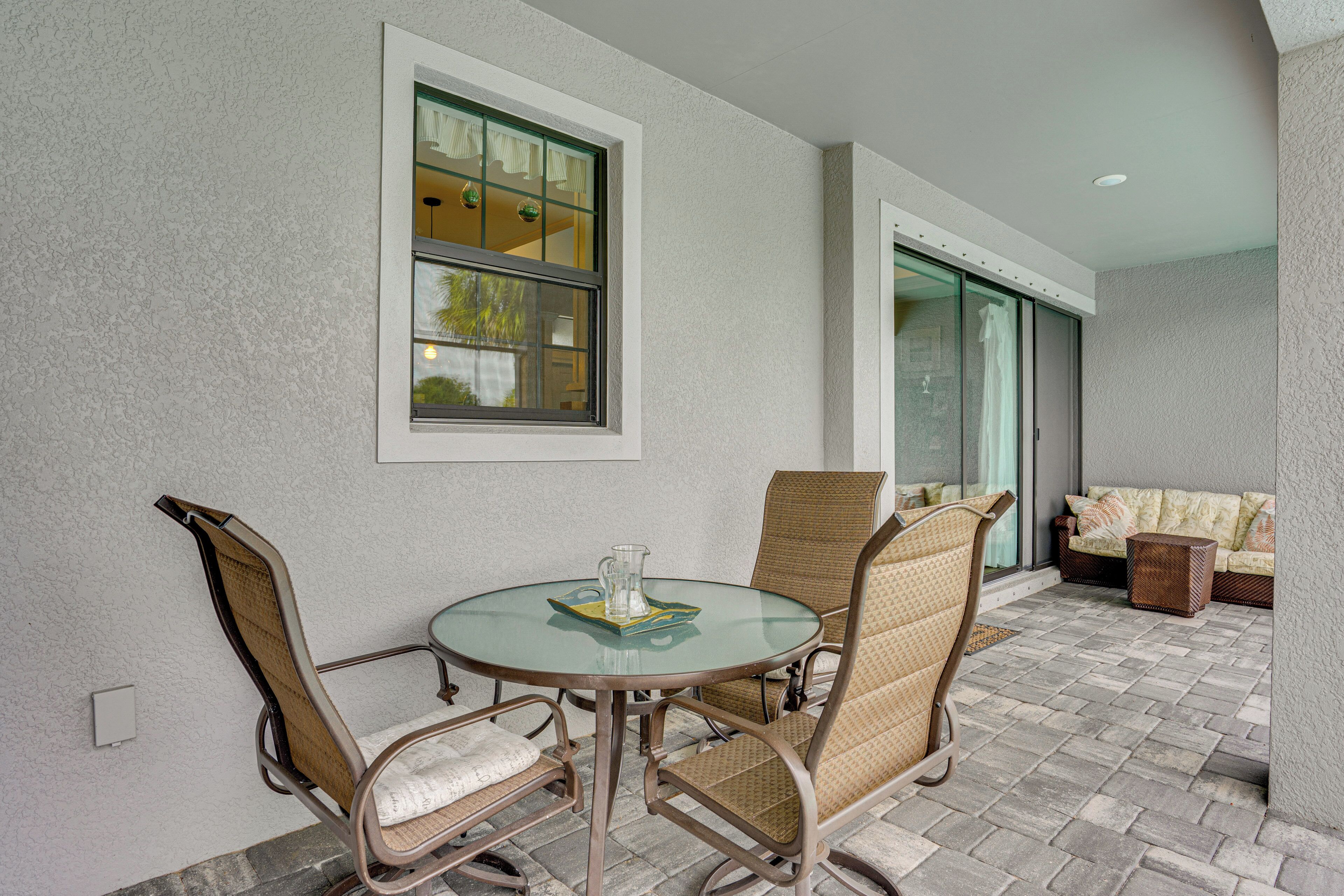 A patio with a round glass table, wicker chairs, a cushioned sofa, and a window with curtains.