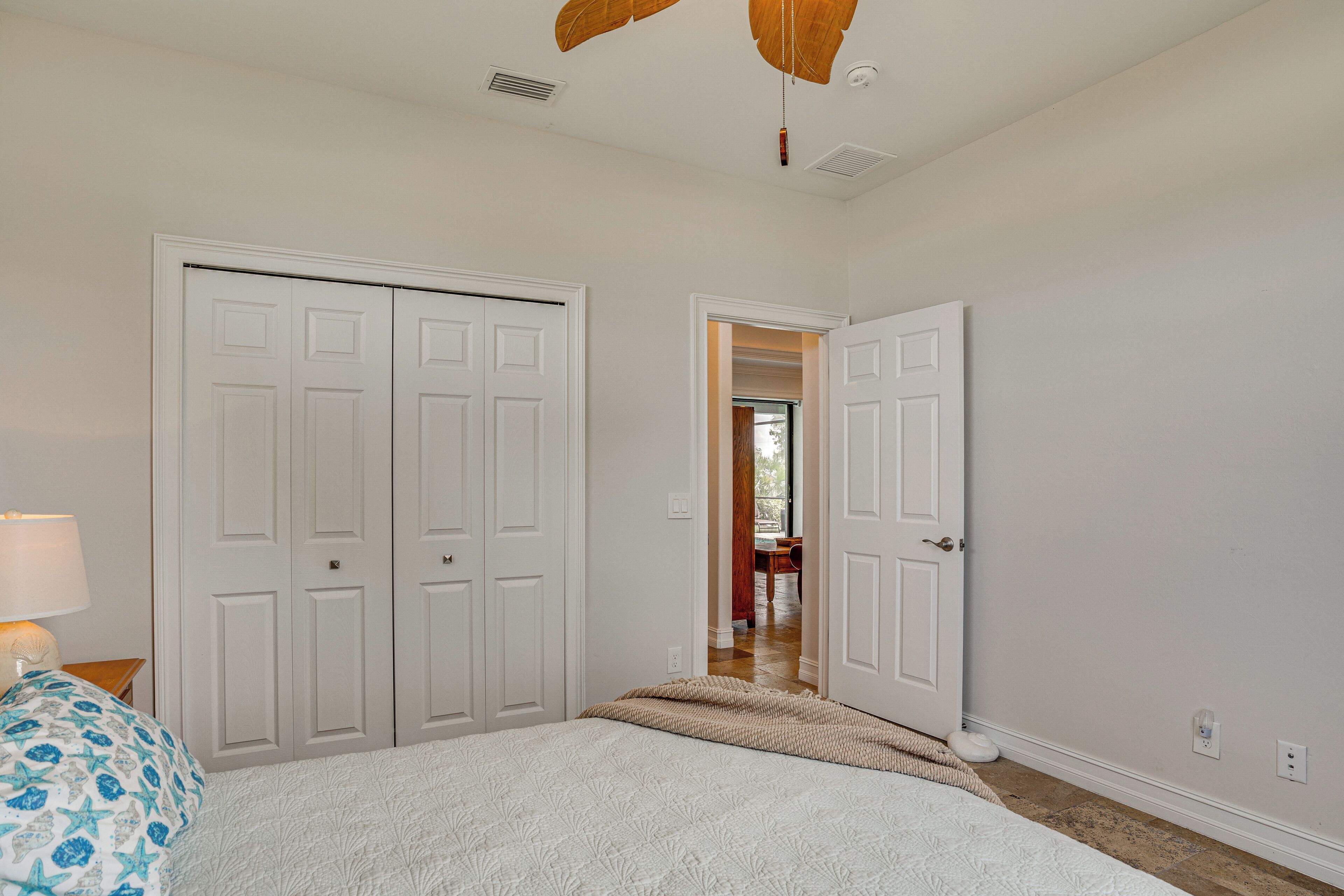 A bedroom with a bed, a nightstand, a lamp, a ceiling fan, and a closet with two doors.