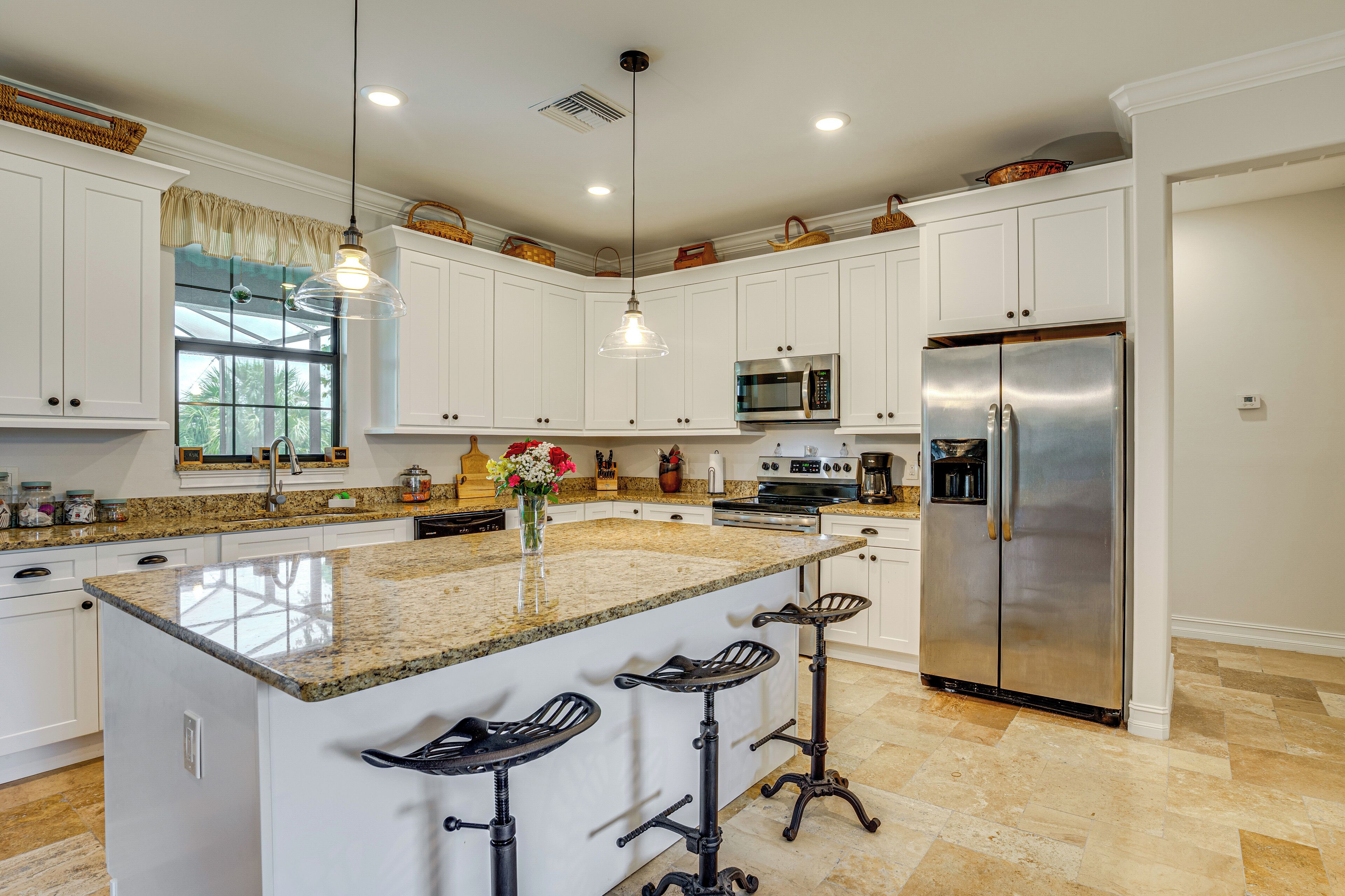 A kitchen with white cabinets, a granite countertop, a stainless steel refrigerator, and a bar stool area.