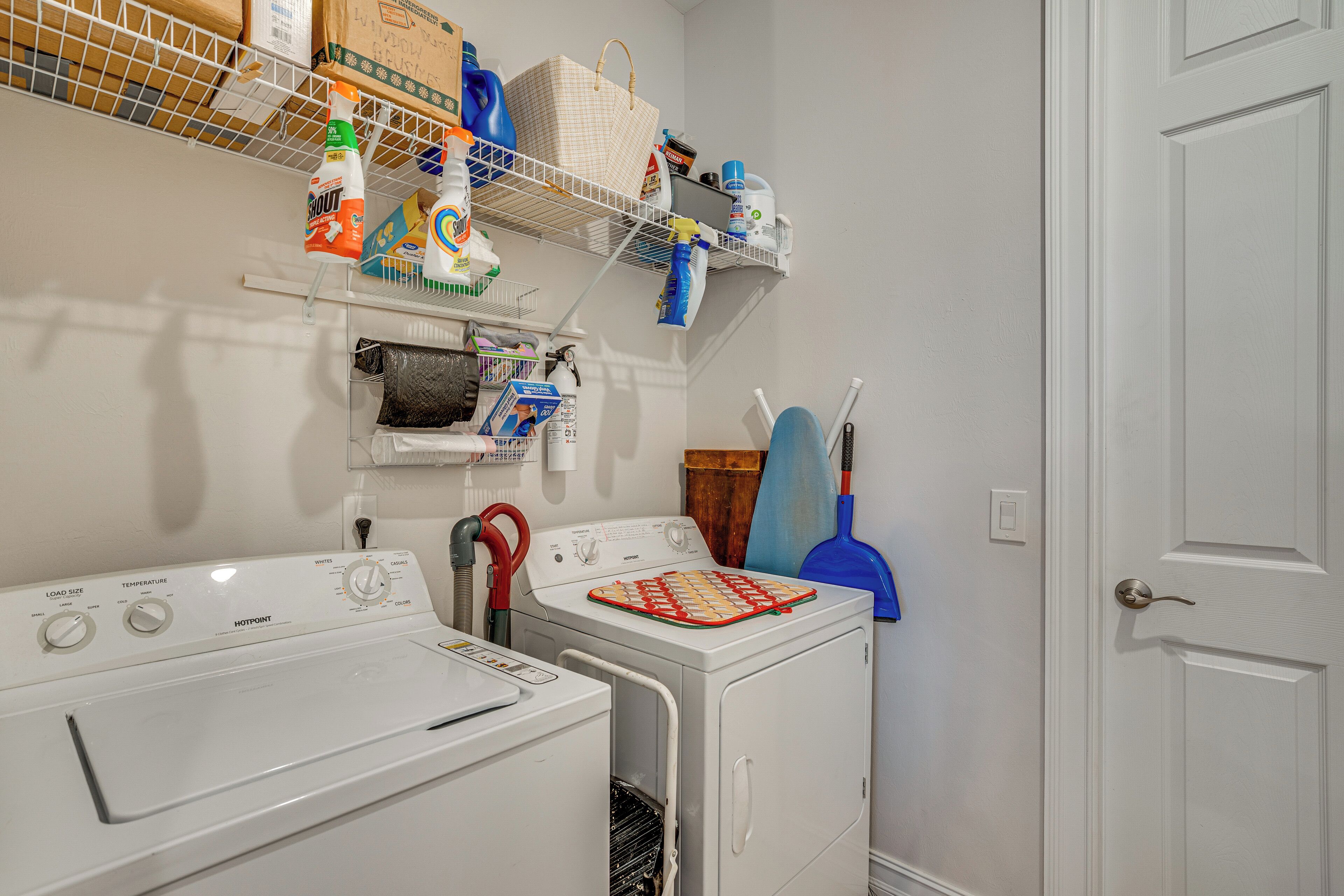 A laundry area with two washing machines, shelves with cleaning supplies, and a door with a handle.