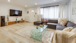 Una sala de estar con un sofá, una mesa de centro de vidrio, un televisor de pantalla plana y un mueble de madera.