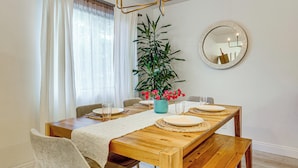 Un comedor con mesa de madera, sillas, un jarrón de flores y un espejo en la pared.
