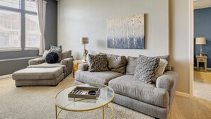 A living room with a grey sofa, ottoman, and a glass coffee table. - Easy E470 & 125 Access! Quiet Englewood Condo (Parker)