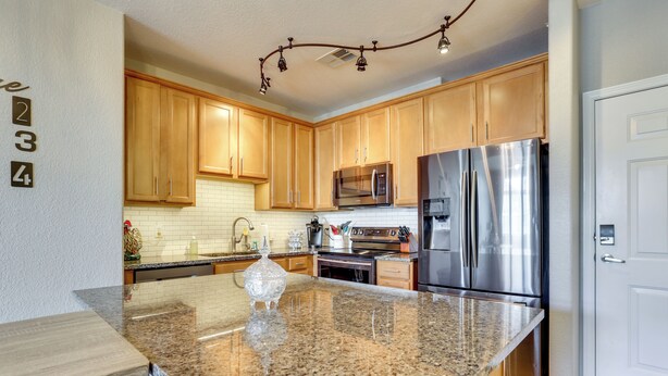 A kitchen with granite countertops, stainless steel appliances, wooden cabinets, and a white door. - Easy E470 & 125 Access! Quiet Englewood Condo (Parker)