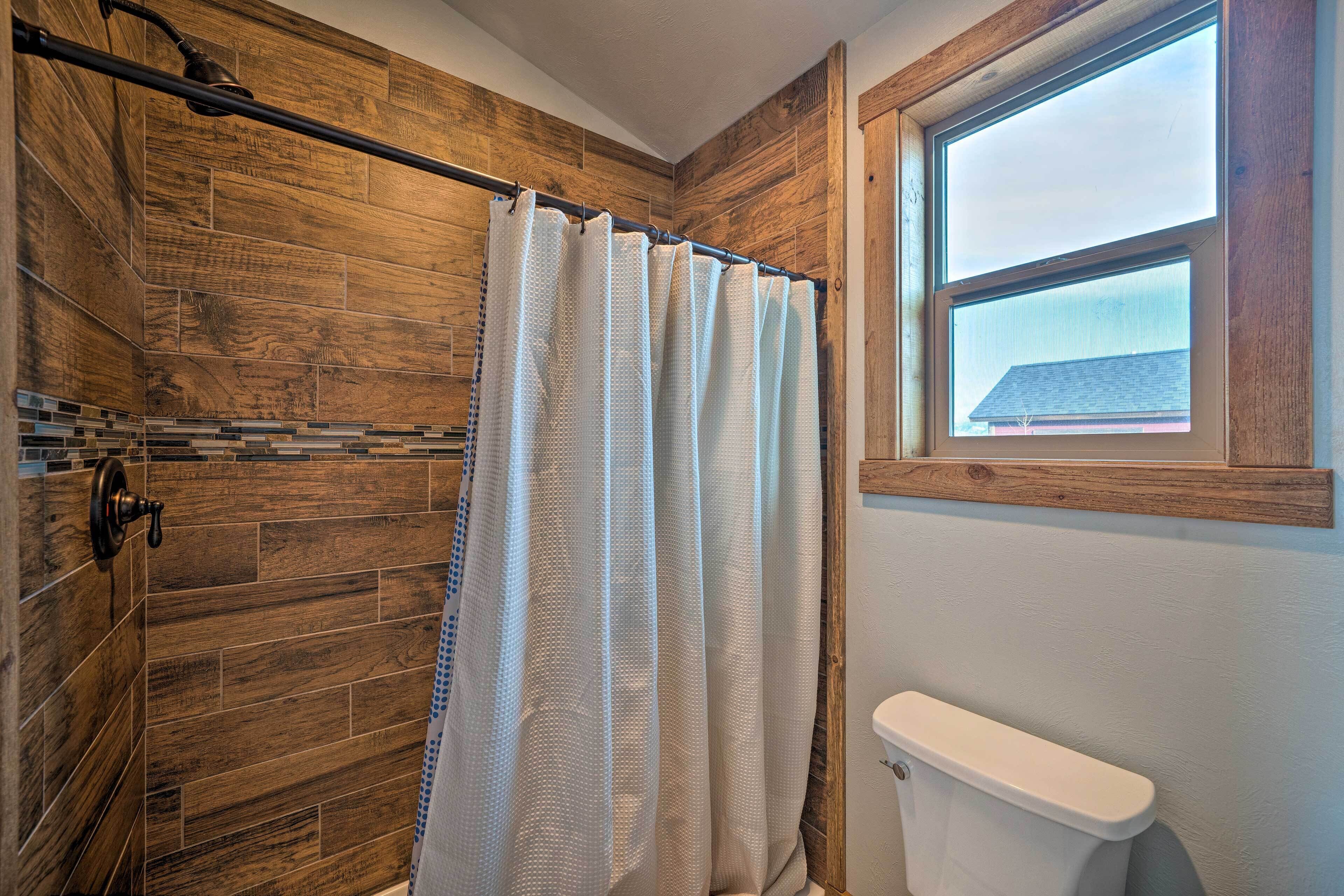 Un baño con paredes de madera, una cortina de ducha, un inodoro y una ventana.