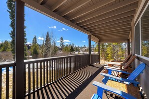 A covered outdoor area with a wooden deck, a railing, and Adirondack chairs.