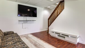 Una sala de estar con un televisor de pantalla plana montado en la pared, una escalera de madera y un mueble de entretenimiento blanco.