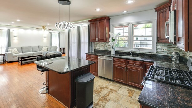 A modern kitchen with dark wood cabinets, a granite countertop, stainless steel appliances, and a dining area with a sofa and table. - 1 Mi to Main St! Family-friendly Reisterstown Home (Reisterstown)