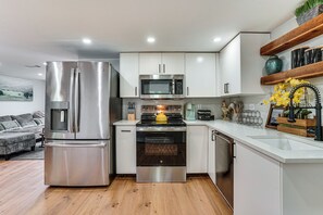 A modern kitchen with stainless steel appliances, white cabinetry, and a wooden floor. - Walk to Historic Weatherford: Home w/ Yard (Weatherford)