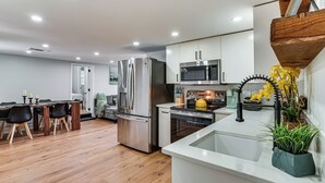 A modern kitchen with stainless steel appliances, a dining area with a wooden table and chairs, and a white countertop with a sink and potted plant. - Walk to Historic Weatherford: Home w/ Yard (Weatherford)