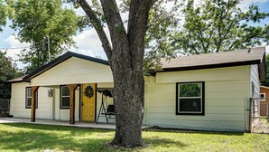 A single-story house with a front porch, a visible garage door, and a tree in the front yard.