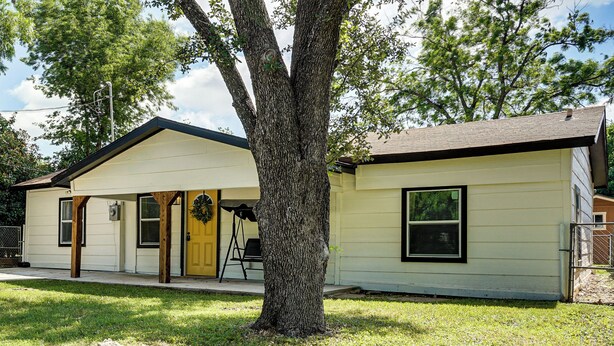 A single-story house with a front porch, a visible garage door, and a tree in the front yard. - Walk to Historic Weatherford: Home w/ Yard (Weatherford)