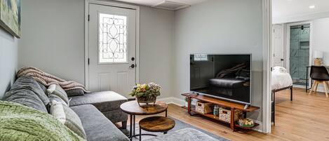 Una sala de estar con un conjunto de sofás, una televisión, una mesita con un jarrón y una puerta con un panel de vidrio decorativo.