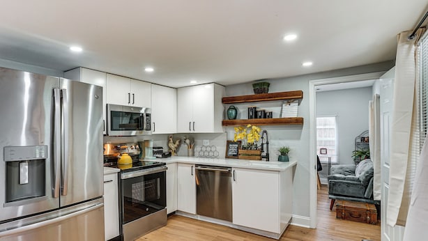 A modern kitchen with stainless steel appliances, white cabinetry, and a wooden floor.