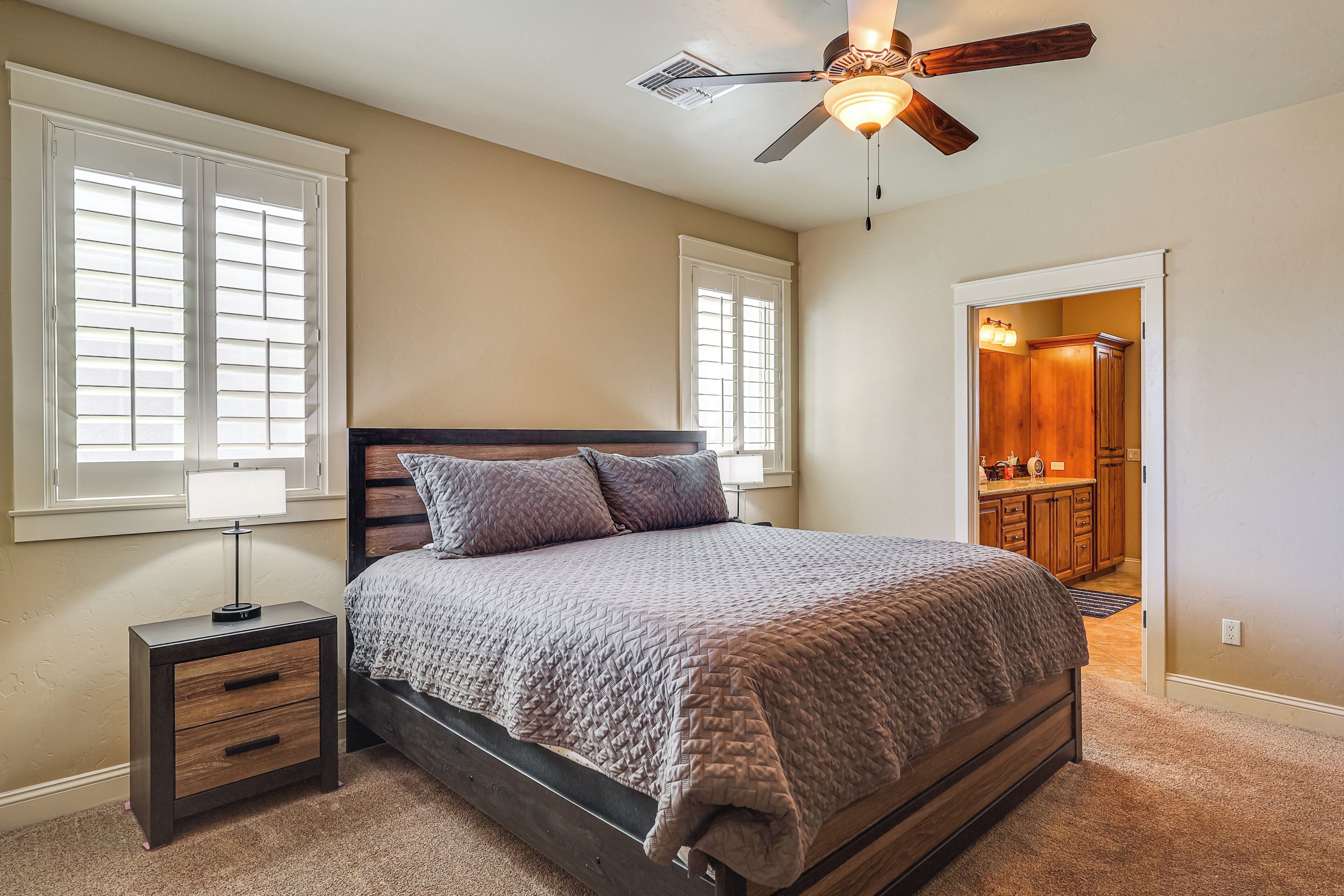 Un dormitorio con cama, mesita de noche, lámpara, ventilador de techo y vistas al baño.