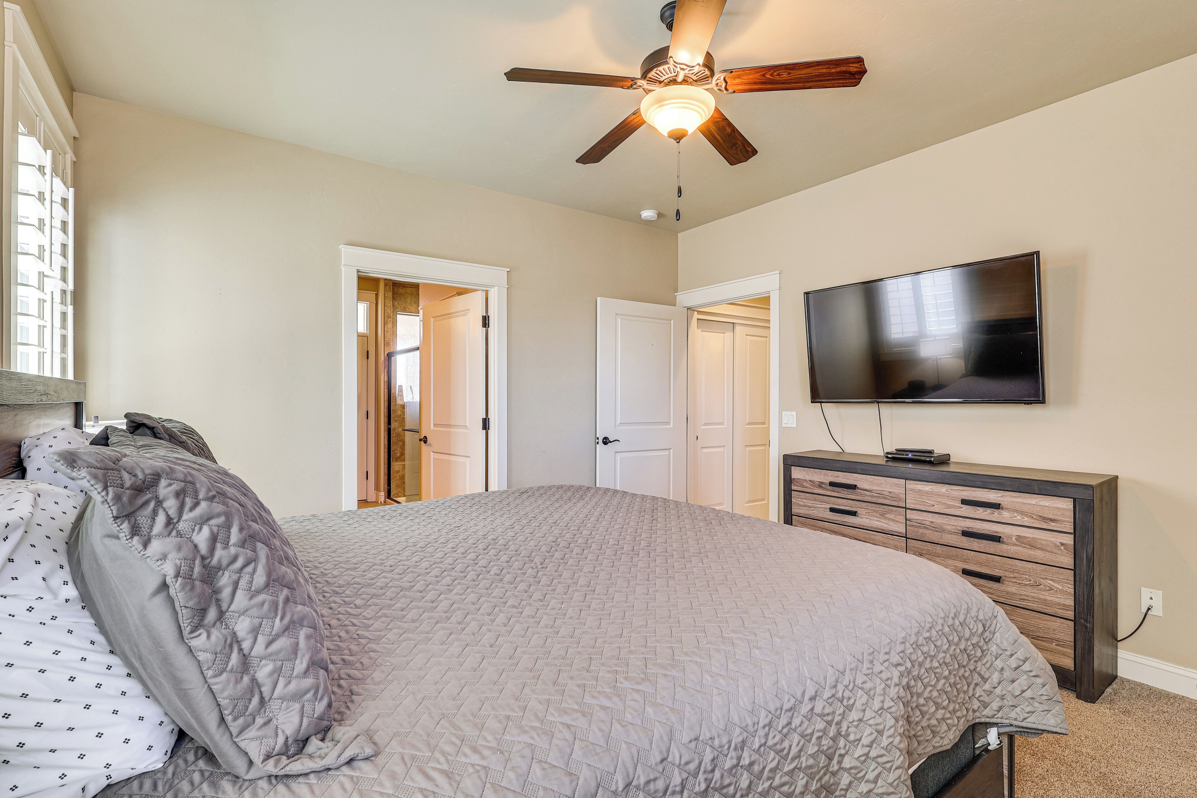 A bedroom with a bed, a ceiling fan, a TV, and a dresser.