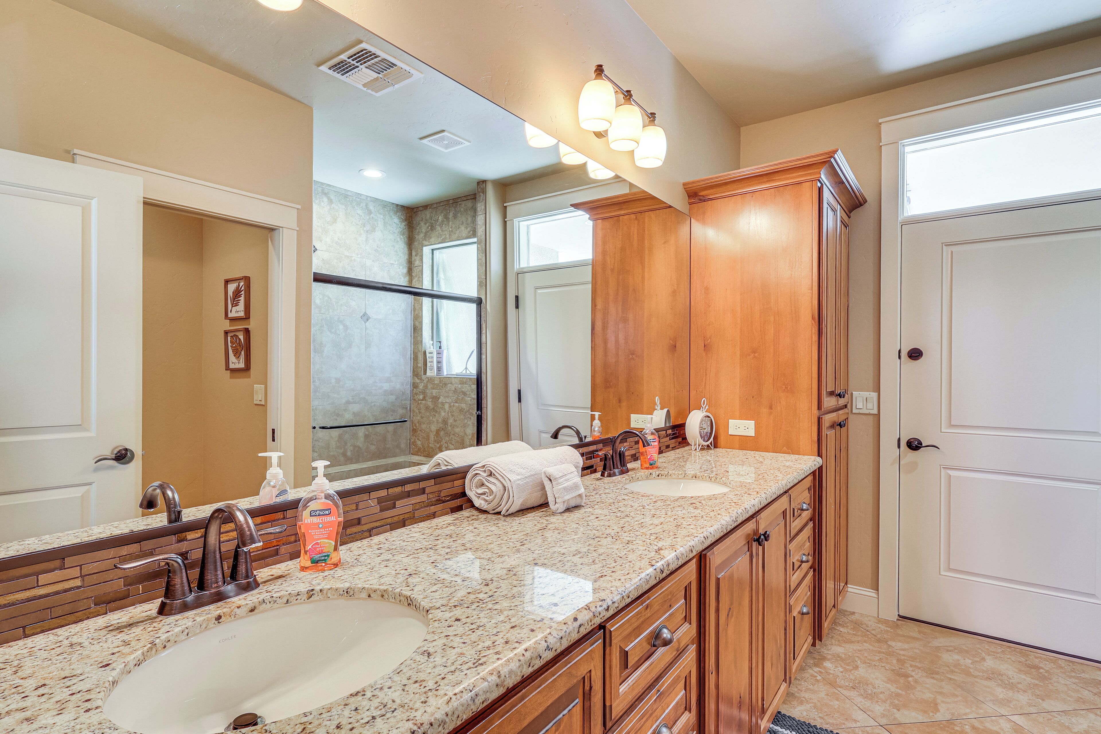 A bathroom with two sinks, a large mirror, wooden cabinets, and a shower area.