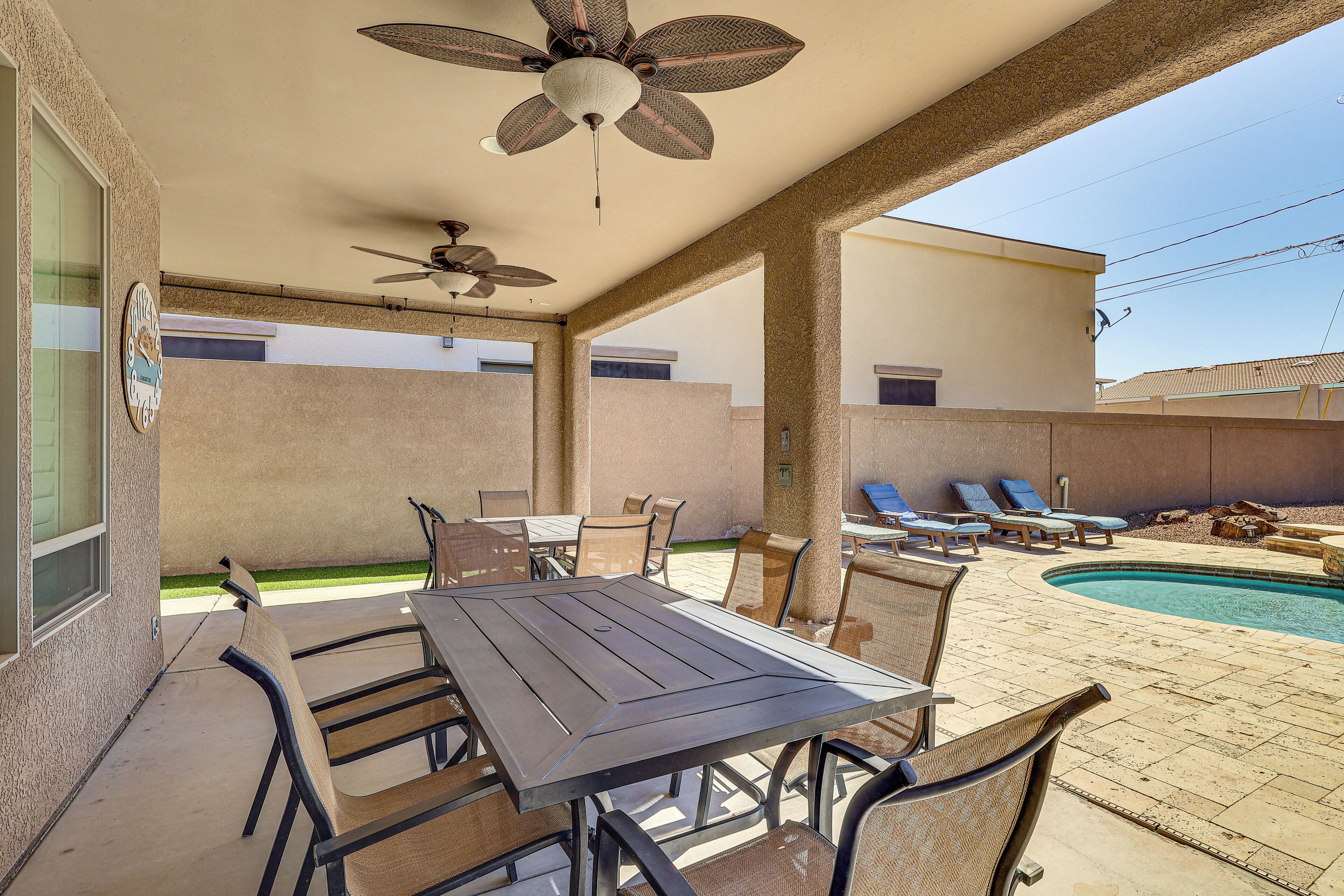 Eine Terrasse im Freien mit Tisch, Stühlen, Deckenventilator, Schwimmbecken und Liegestühlen.